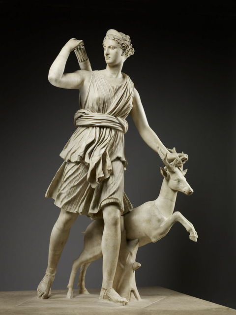 Marble statue picturing goddess Artemis. Poised with her left foot in front, she uses her right hand to reach for a quiver of arrows. Her other hand hovers above the horns of a deer standing on its' hind legs.